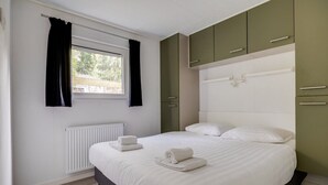 A bedroom with a bed, white curtains, a window, a radiator, and green cabinets.