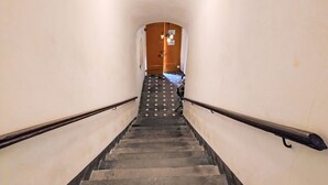 Un escalier étroit, muni d’une main courante de chaque côté, menant à une porte située en haut.