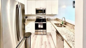 A modern kitchen with stainless steel appliances, white cabinets, and a light wood floor. - Luxury and comfy GS condo on the first floor. (Gulf Shores)