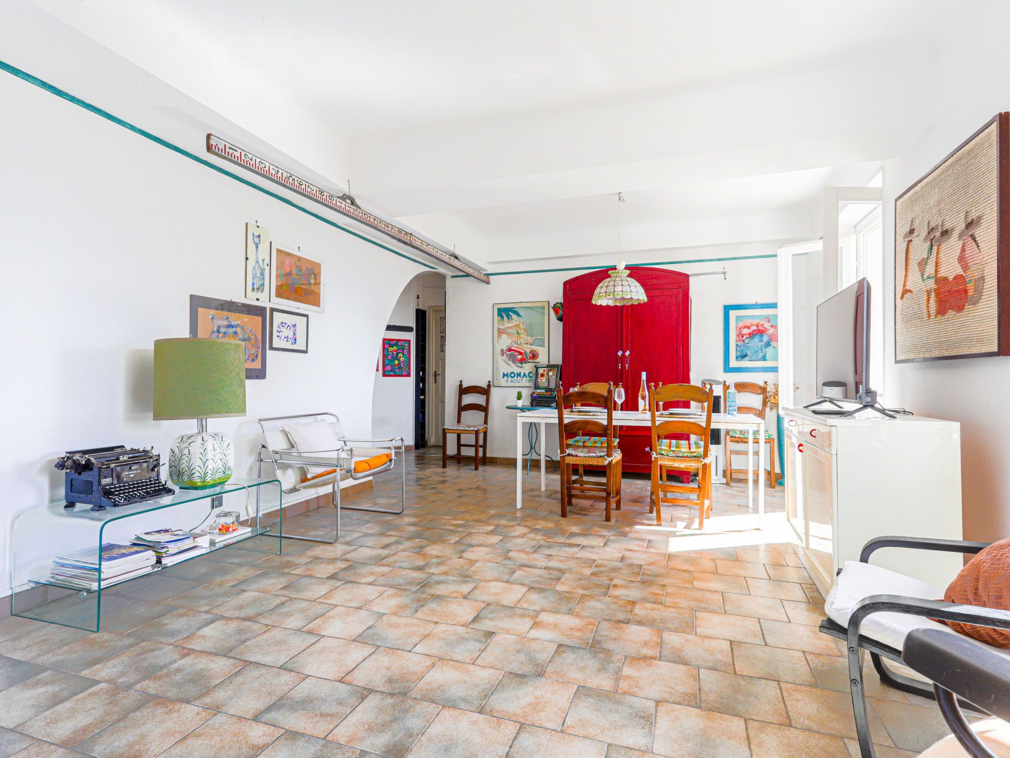 A spacious living room with a tiled floor, a glass coffee table, a red cabinet, and a television.