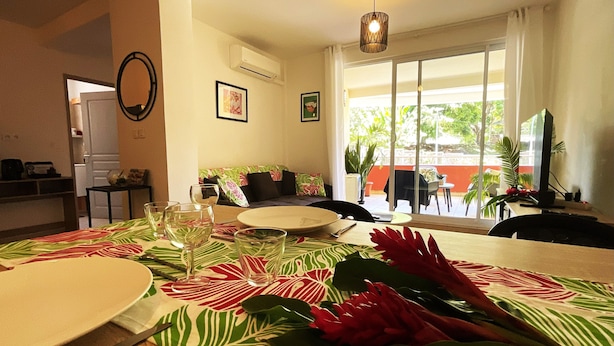 A dining area with a table set for two, a sofa, and a view of the outdoors. - Prestige Lodging Papeete (Papeete)