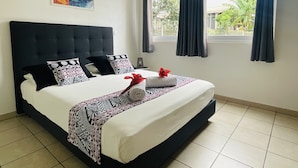 A neatly made bed with patterned bedding, a dark headboard, and a painting on the wall. - Prestige Lodging Papeete (Papeete)