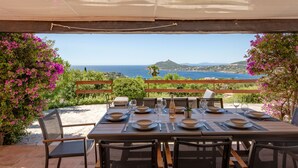 Un área de comedor al aire libre con una mesa dispuesta para seis personas, con vistas a un paisaje costero.