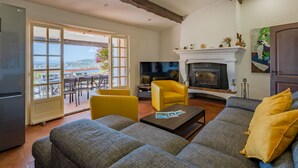 Una sala de estar con chimenea, un conjunto de sofás, un sillón amarillo y un televisor.