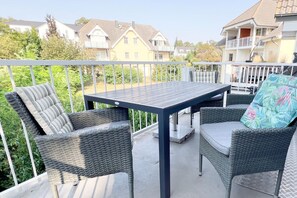Un balcon doté de meubles en osier et d’une table, offrant une vue sur un quartier résidentiel avec ses maisons et sa verdure.