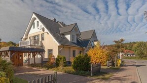 Ein zweigeschossiges Haus mit einem Balkon, einer Veranda und einem gepflasterten Einfahrt.