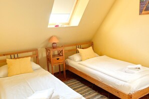 Une petite chambre accueillante avec deux lits simples, une table de chevet avec une lampe et une lucarne.