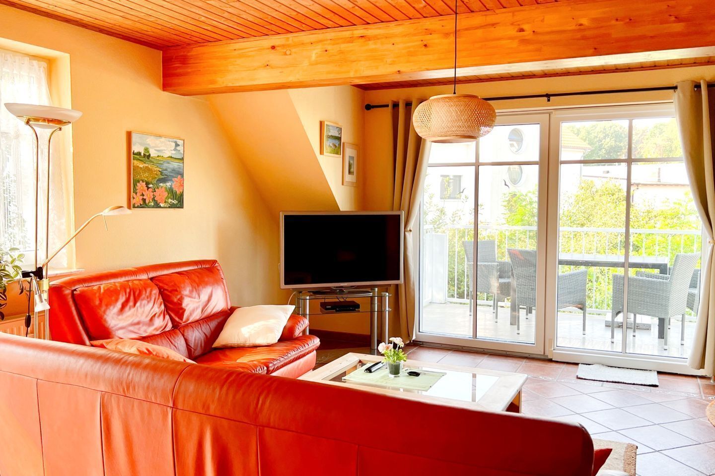 Ein Wohnzimmer mit einem roten Ledersofa, einem Flachbildfernseher und einer großen Schiebeglastür, die auf eine Terrasse im Freien führt.