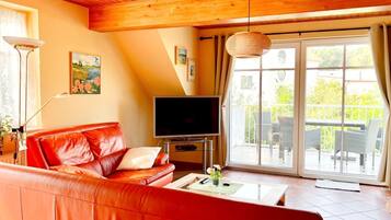 Ein Wohnzimmer mit einem roten Ledersofa, einem Flachbildfernseher und einer großen Schiebeglastür, die auf eine Terrasse im Freien führt.