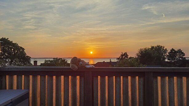 A sunset view from a wooden deck with a railing, overlooking a body of water and trees.