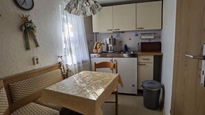 A compact kitchen with a dining area, including a table with a floral tablecloth, a wooden chair, and a clock on the wall.