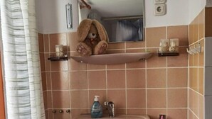 A bathroom with a pedestal sink, a mirror, a shelf with toiletries, a trash bin, and a towel rack.