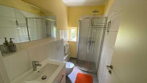 Et moderne badeværelse med hvid vask, spejl, toilet og brusekabine med glasvægge.