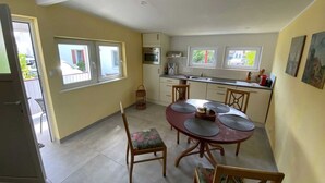 Et kompakt køkken med spiseplads, med et rundt bord med fire stole, indbygget ovn og et vindue med udsigt til gaden.