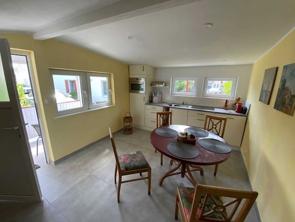 A compact kitchen with a dining area, featuring a round table with four chairs, a built-in oven, and a window overlooking the street.
