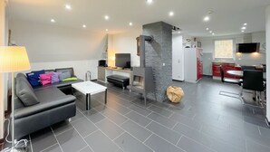 A modern living room with a sofa, a coffee table, and a fireplace. There is a kitchen area with red cabinets and a dining table. - Meeresbrise - Stilvoll Genießen, auf 80qm, für bis zu 4 Personen, auf der Sonneninsel Usedom (Loddin)