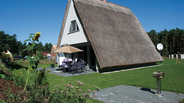 A house with a sloped thatched roof, a patio with outdoor furniture, and a satellite dish. - Meeresbrise - Stilvoll Genießen, auf 80qm, für bis zu 4 Personen, auf der Sonneninsel Usedom (Loddin)