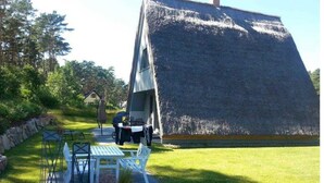 A thatched-roof building with a small patio area featuring a table and chairs. - Meeresbrise - Stilvoll Genießen, auf 80qm, für bis zu 4 Personen, auf der Sonneninsel Usedom (Loddin)