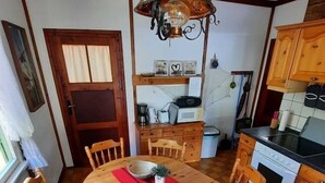 Una mesa de comedor de madera con sillas, un mantel individual rojo y una lámpara colgante en una cocina con armarios de madera y suelo de baldosas.