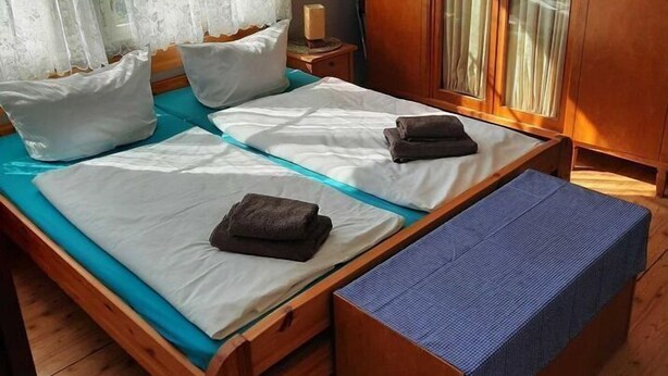 Una cama de madera con ropa de cama blanca y un banco, un armario con puertas de cristal y cortinas de gasa.