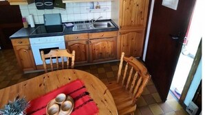 Una cocina con armarios de madera, una estufa y un lavabo. Hay una mesa de comedor con sillas y un mantel individual rojo.