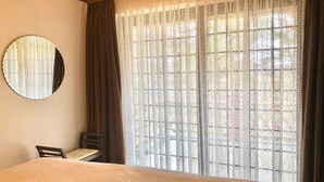 A room with a bed, a chair, a round mirror, and a window with lace curtains. - Strandstrasse - "Vacation in the vacation home Min Hüsung: relaxation and adventure on the Baltic Sea!" (Loddin)