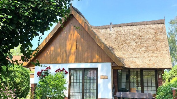 A wooden building with a thatched roof, a brick foundation, and a large window. - Strandstrasse - "Vacation in the vacation home Min Hüsung: relaxation and adventure on the Baltic Sea!" (Loddin)