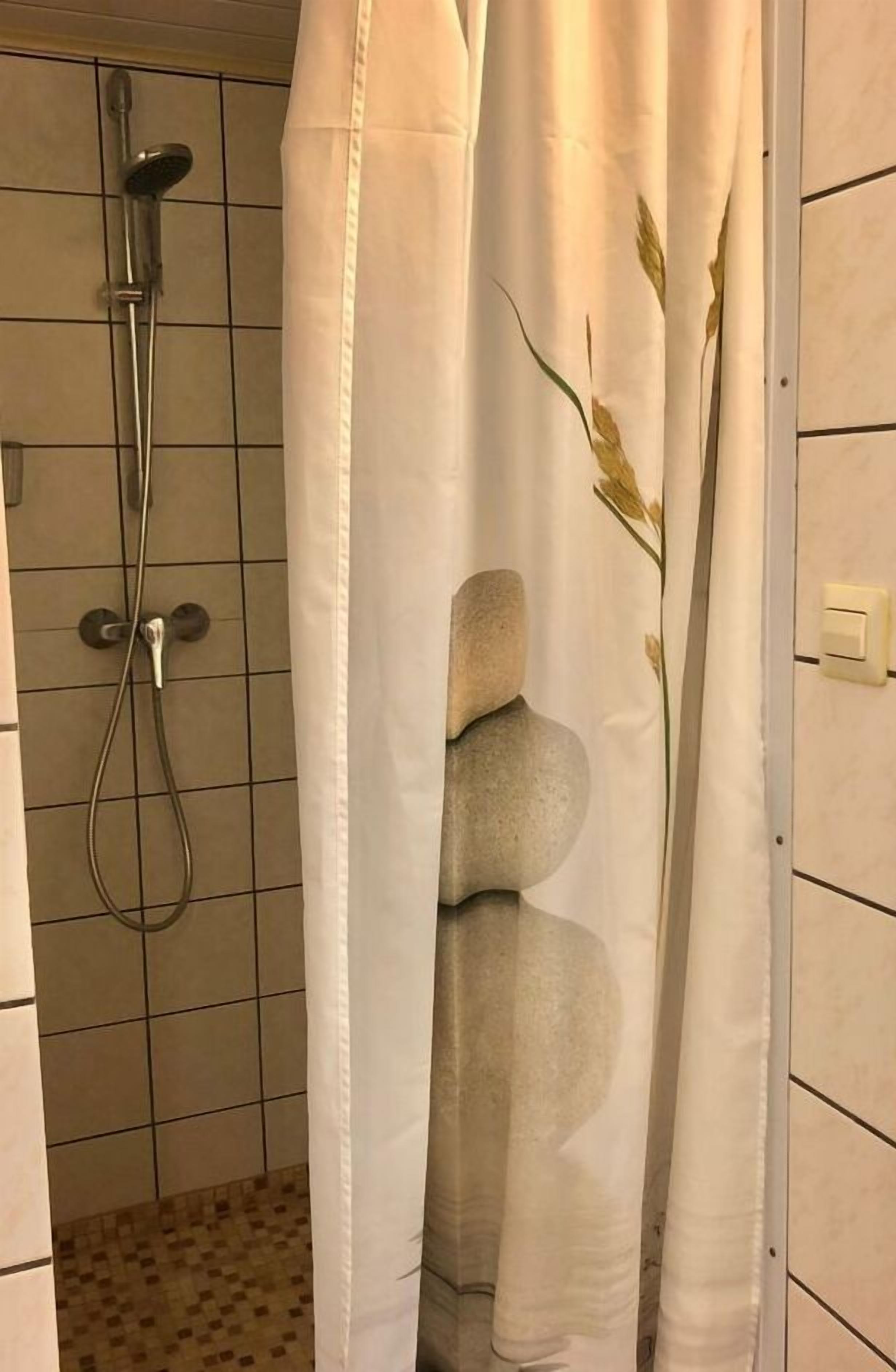 En duschhörna med ett vitt duschdraperi som har ett mönster med staplade stenar.