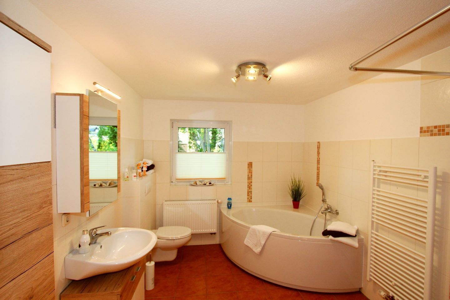 Une salle de bain avec un lavabo, des toilettes et une baignoire. Il y a une fenêtre au-dessus des toilettes et un porte-serviettes à côté de la baignoire.