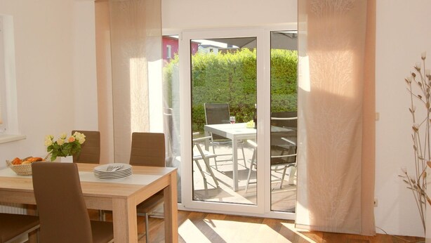 Uma sala de jantar com mesa, cadeiras e vista para um pátio externo também com mesa e cadeiras.