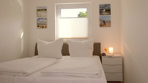Quarto de hotel com cama, mesa de cabeceira com abajur e janela com persianas.