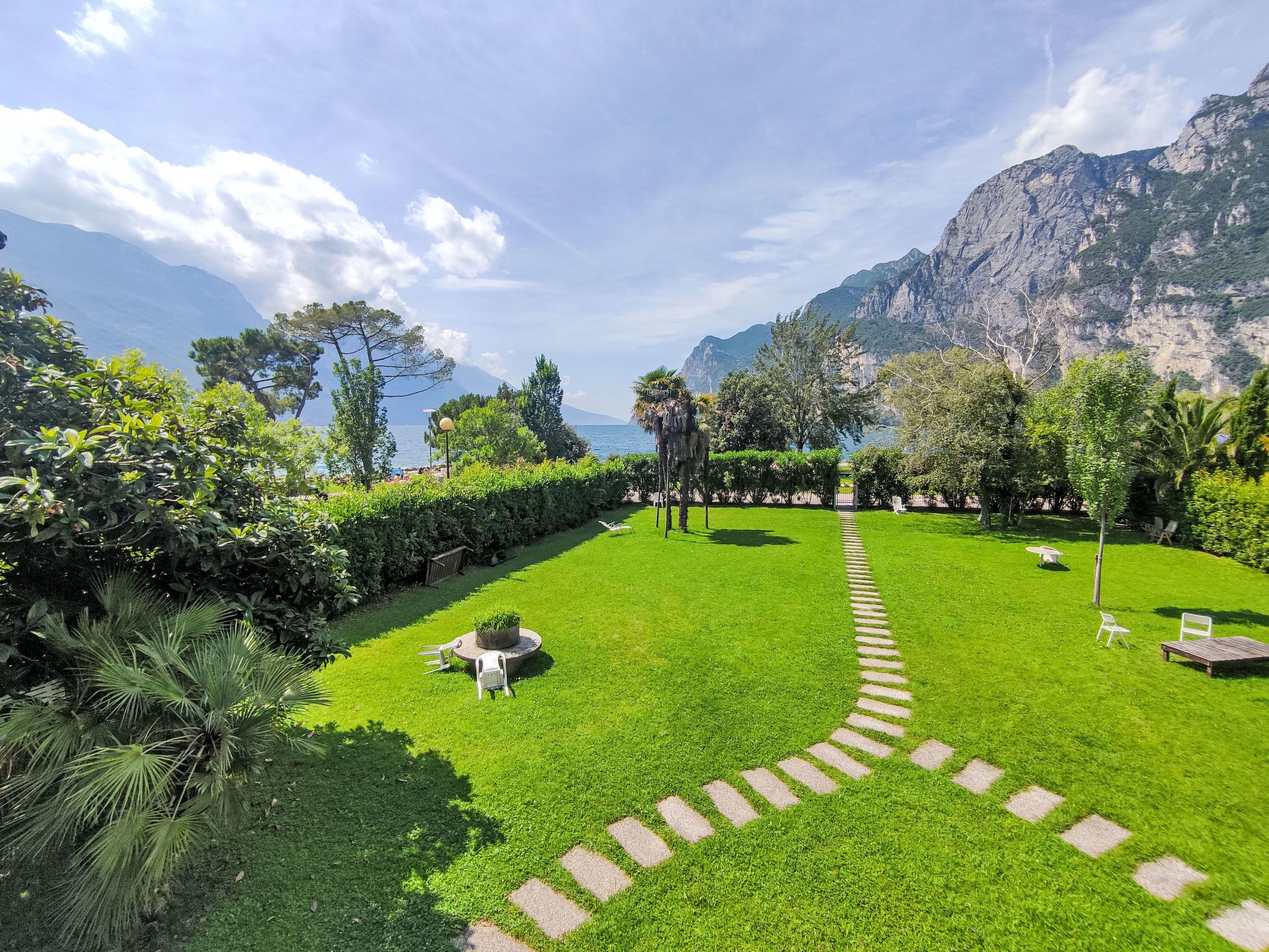 A well-maintained garden with a stone pathway leading to a seating area, surrounded by lush greenery and a view of a mountainous coastline.