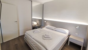A modern hotel room with a large bed, bedside tables, a mirror, and a door.