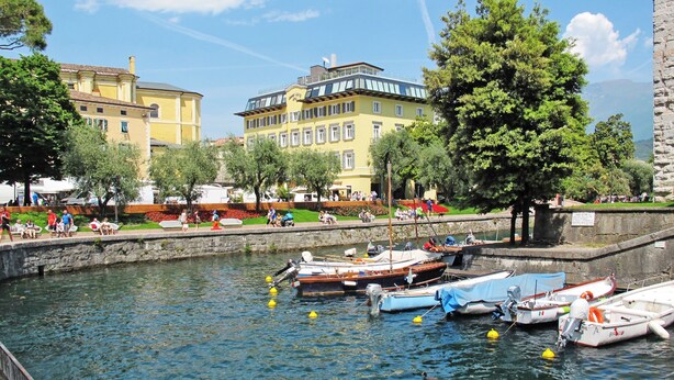 A canal with boats, a stone wall, and buildings with balconies.