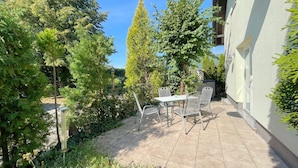 Un patio con tavolo e sedie, circondato da alberi e un edificio.