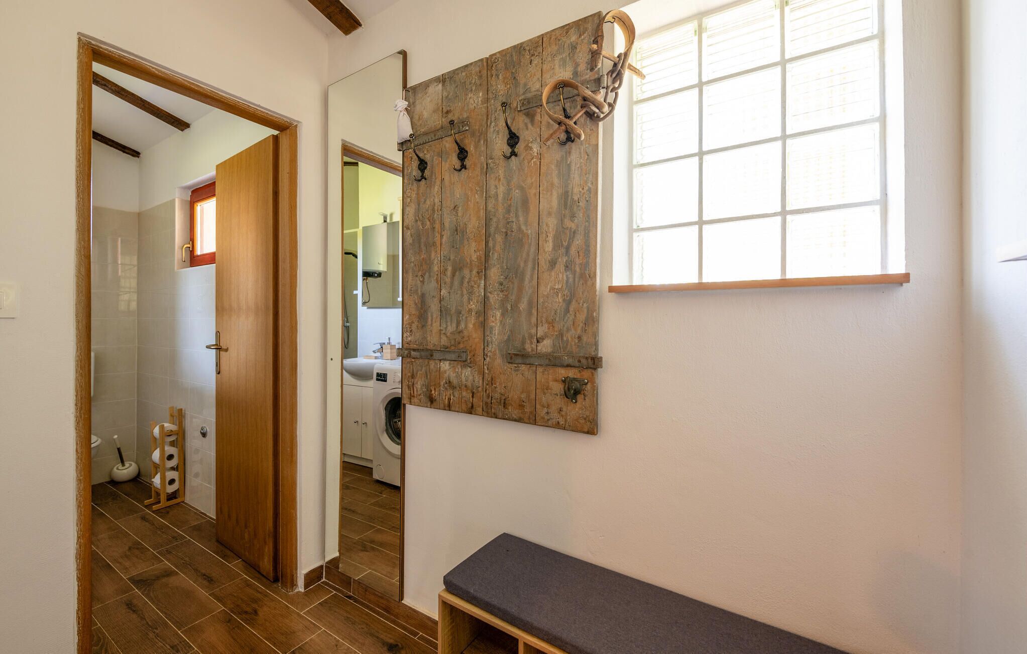 A hallway with a wooden bench, a washing machine, and a large mirror with rustic decor.