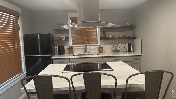 A modern kitchen with a central island, dark chairs, and a black refrigerator. - Cozy apartment in Pendleton Oregon  (Pendleton)