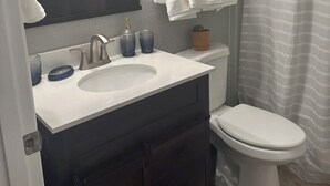 A bathroom with a white sink, dark cabinets, a white toilet, and a shower curtain. - Cozy apartment in Pendleton Oregon  (Pendleton)