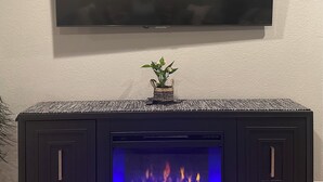 A modern living room with a flat-screen TV mounted on the wall, a dark wood console table with a small plant, and a built-in fireplace with blue flames. - Cozy apartment in Pendleton Oregon  (Pendleton)