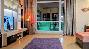 A living room with a television, a purple rug, and a sliding glass door leading to a balcony. - Sunny Beach Serenity Apartment (Sunny Beach)