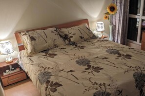 A bedroom with a floral bedspread, two bedside lamps, a nightstand, and a window with curtains. - Sunny Beach Serenity Apartment (Sunny Beach)