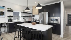 Une cuisine moderne avec des meubles de couleur noire, des appareils en acier inoxydable et un îlot central doté de tabourets de bar.