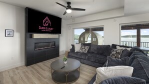 Un salon moderne doté d’un téléviseur à écran plat, d’une cheminée, d’un ventilateur de plafond, d’une grande fenêtre offrant une belle vue et d’un coin salon confortable.