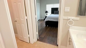 A hallway leading to a bedroom with a bed, a nightstand, and a lamp. There is a bathroom with a sink and mirror. - Spacious 5bed Houston Retreat Home
6 guests 4 bedrooms 5 beds 3 baths (Houston)