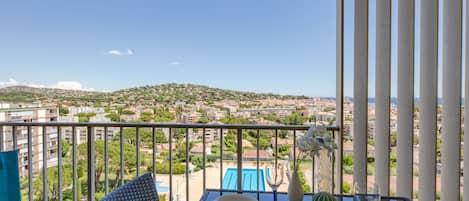 A balcony with a table set for dining, overlooking a cityscape and a hill.