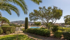 A landscaped garden with a swimming pool, a tall cypress tree, and a view of a hillside town. - Les Côteaux du Préconil by Interhome (Sainte Maxime)