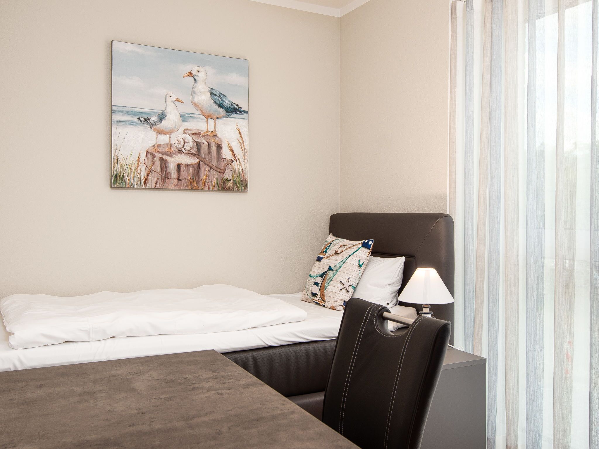 Een hotelkamer met een bed, een bureau, een stoel, een lamp en een schilderij van meeuwen aan de muur.