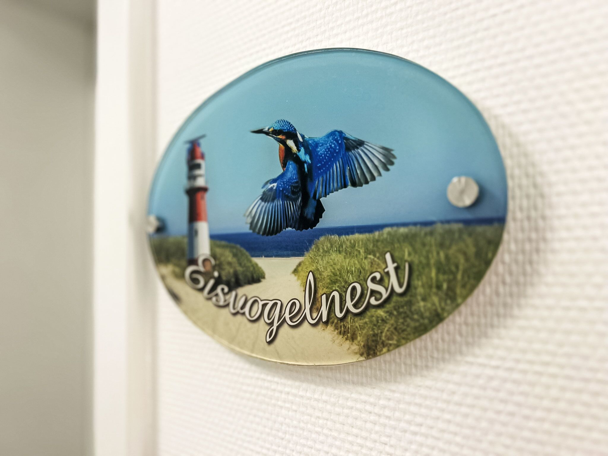 A decorative button with a bird and lighthouse, labeled "Eisjogelnest".