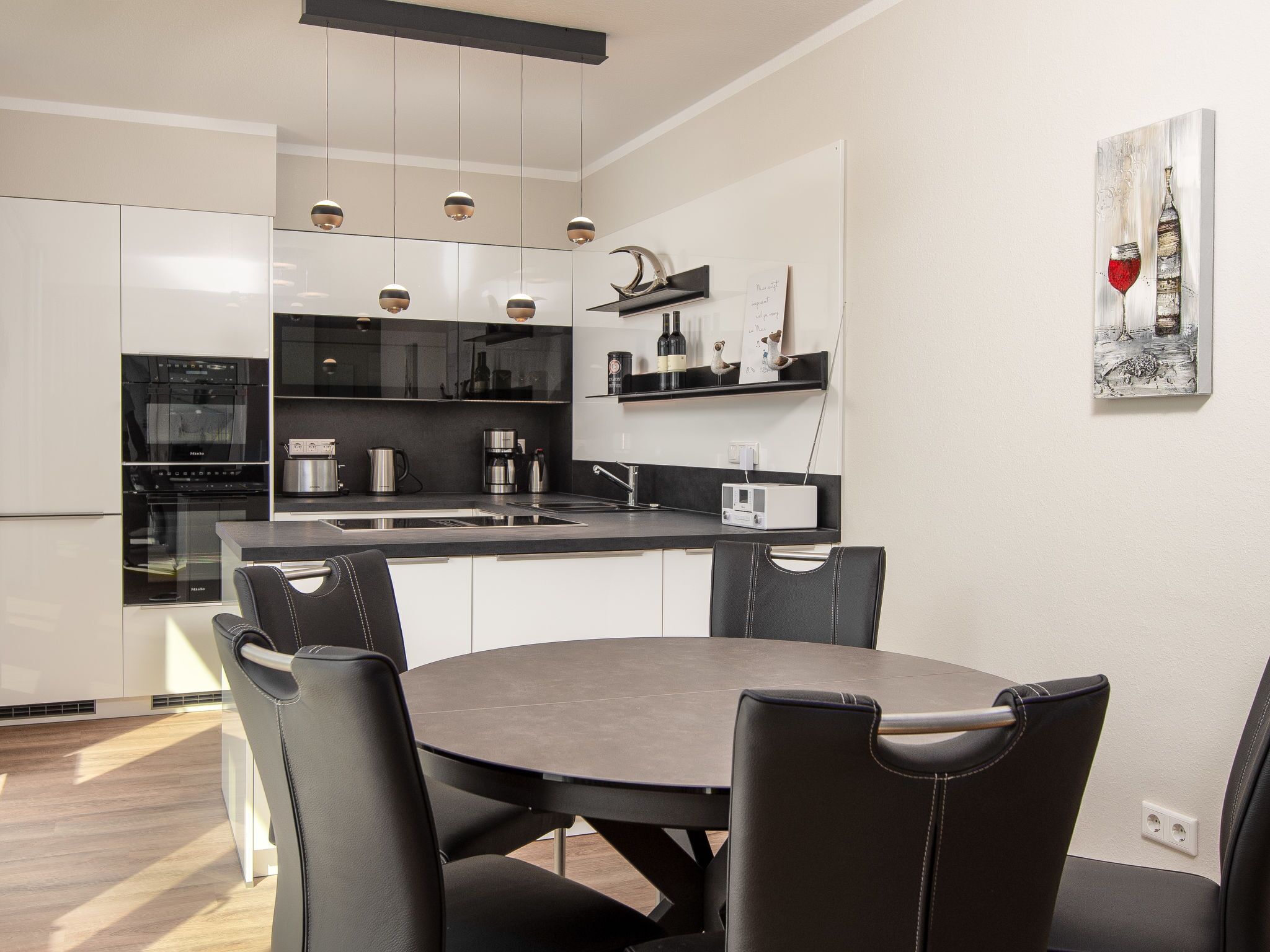 A modern kitchen with a dining area, featuring a black and white color scheme, stainless steel appliances, and pendant lighting.
