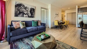 A modern living room with a dark blue sofa, a colorful rug, and a dining area with yellow chairs. - Blue River Parkway’s Colorful Escape (Silverthorne)